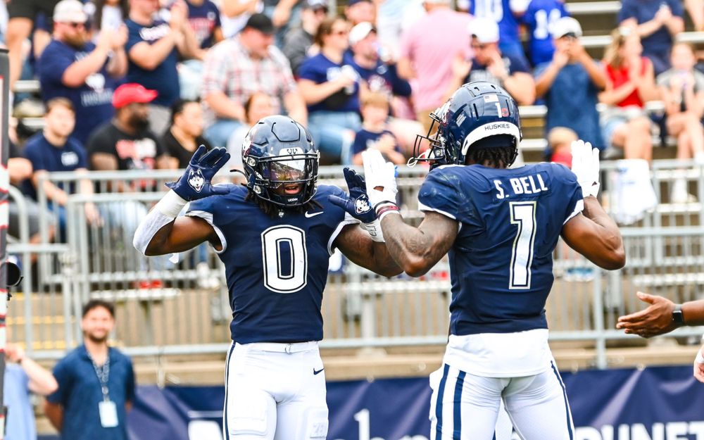 Two football players in navy uniforms celebrate after scoring play.