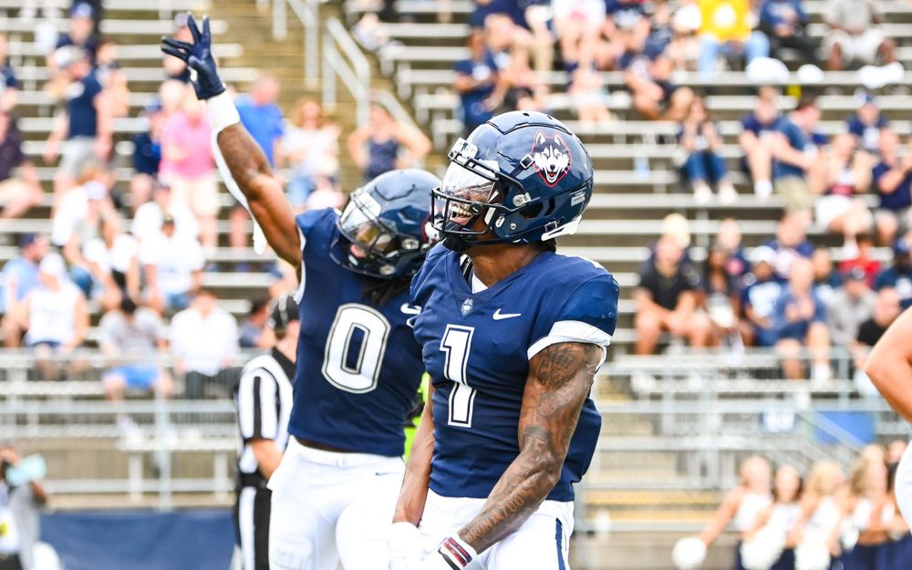 Two players in navy jerseys celebrate together during football game.