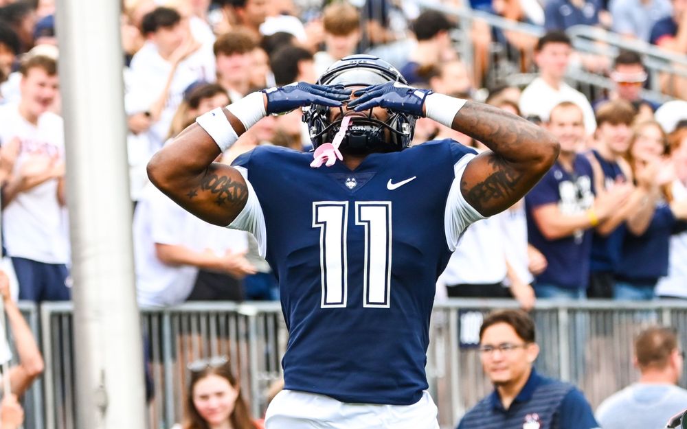 Football player wearing navy jersey number 11 celebrates with arms raised.