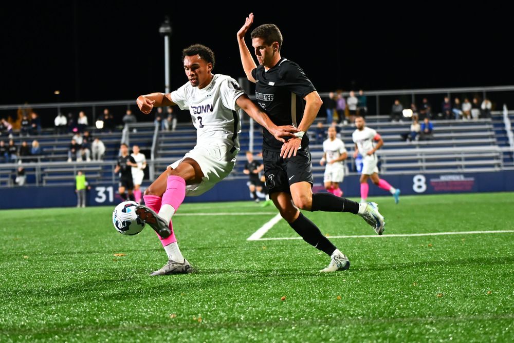 Soccer players battle for possession of the ball during a nighttime match on an artificial turf field.