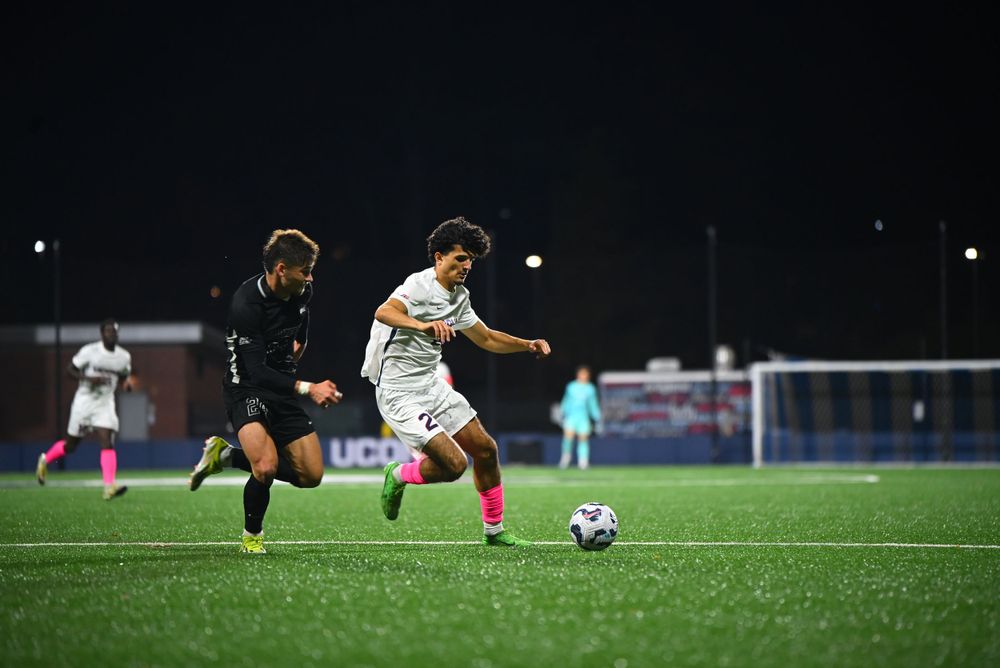Two soccer players compete for the ball during a nighttime match under bright stadium lights.