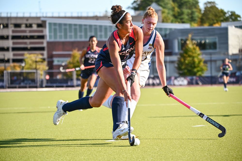 Field hockey player dribbles the ball on an artificial turf field during a match.