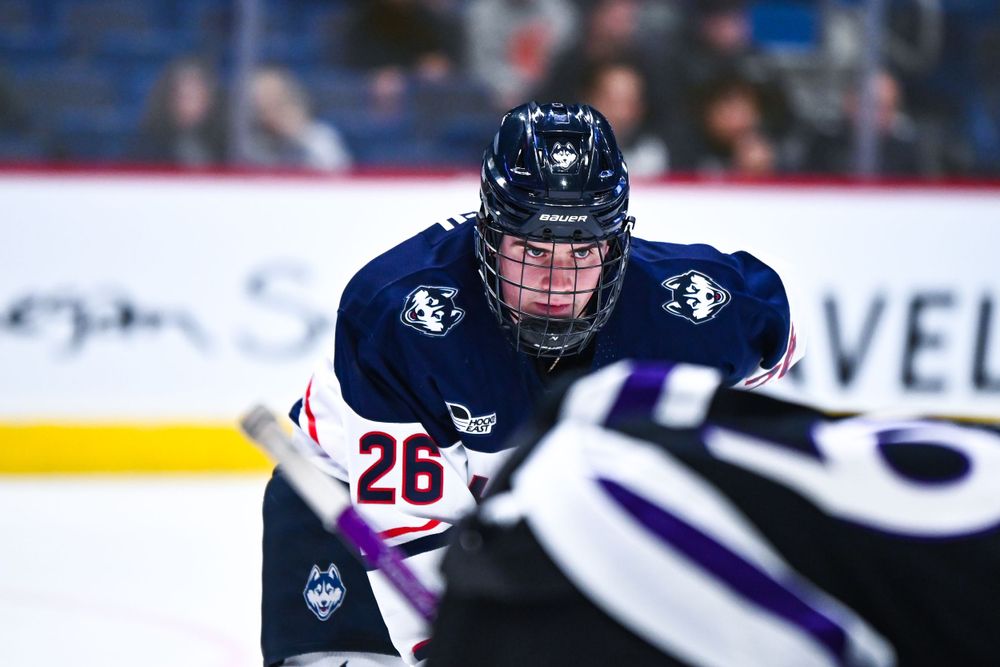 Ice hockey player in navy blue jersey skates during competitive game.