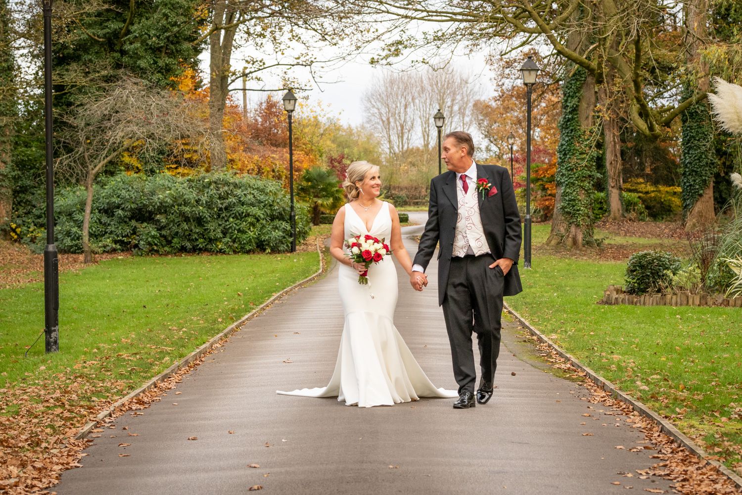 A newly married couple walk up the drive of MacDonald Craxton Wood Hotel in their wedding attire. North Wales Wedding Photographer