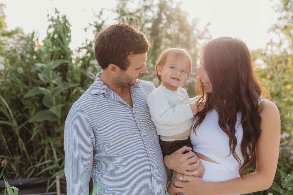 Happy family posing outdoors together at sunset with green foliage in background.