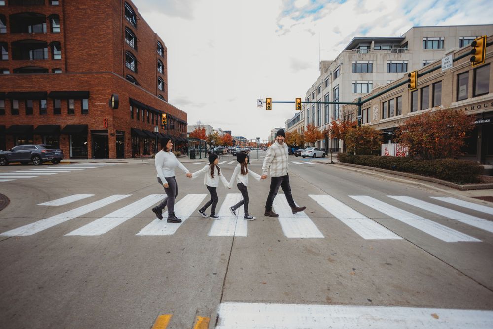 Three people recreating the iconic Beatles Abbey Road album cover while crossing a crosswalk in a city street.