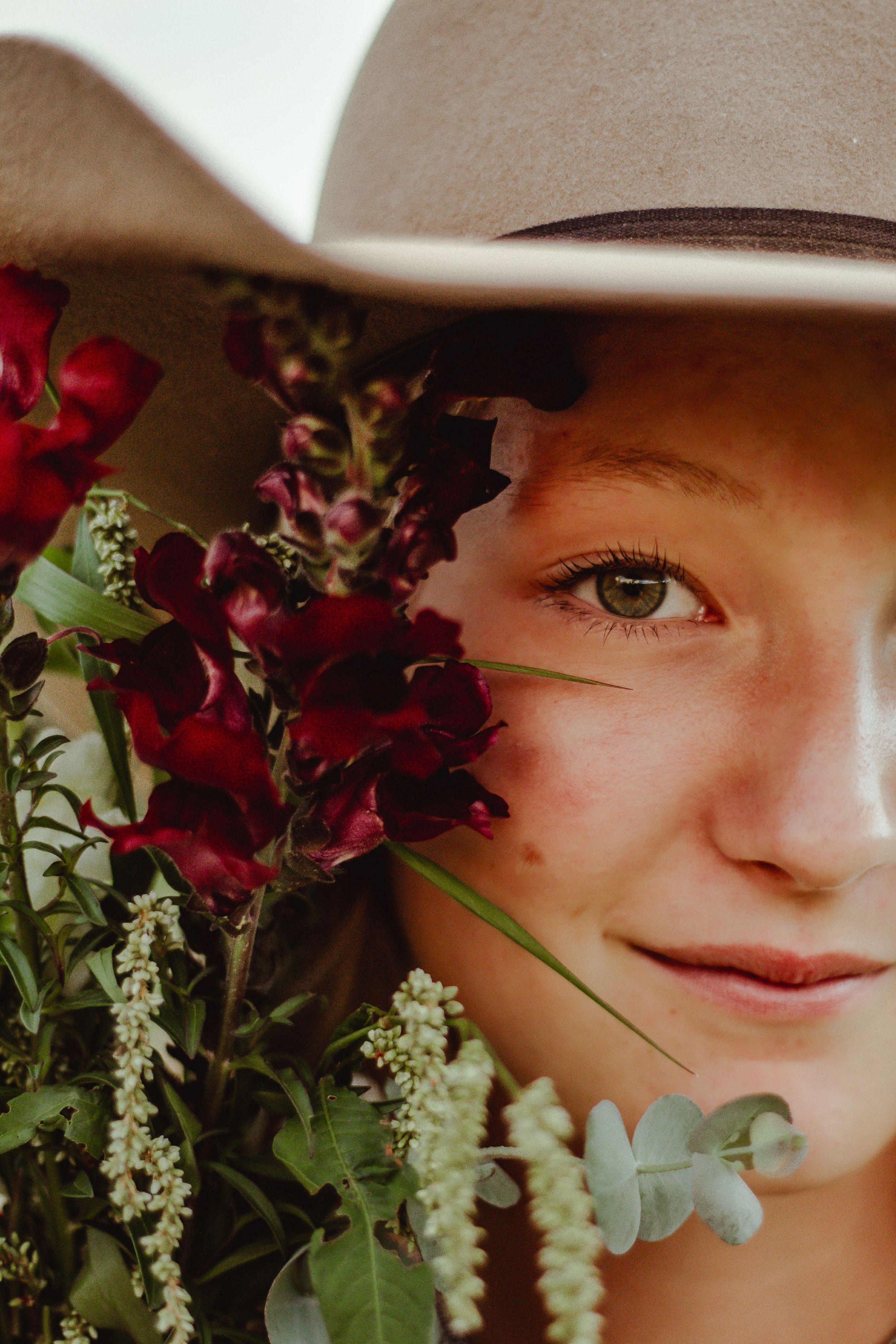 Close-up artistic portrait with red roses and white flowers framing the composition against a soft background.