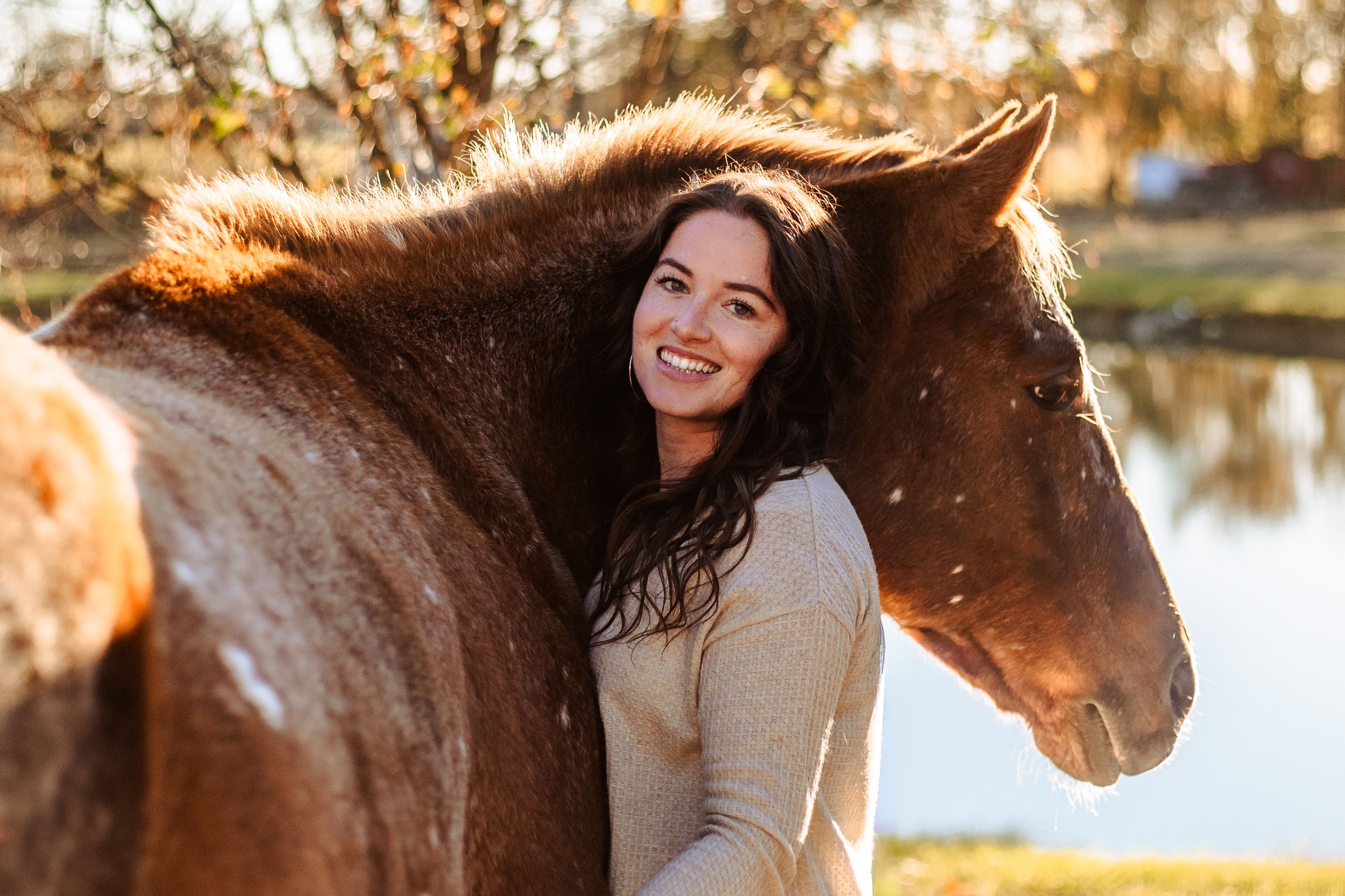 A chestnut horse and rider share a tender moment in golden sunlight during an autumn outdoor photoshoot.