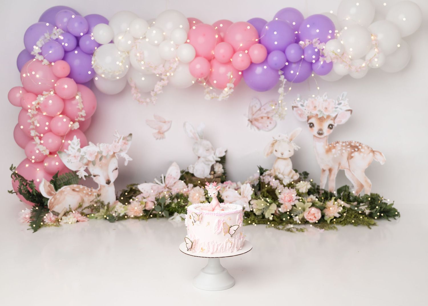 Pink and purple woodland first birthday cake smash setup with florals and balloons.