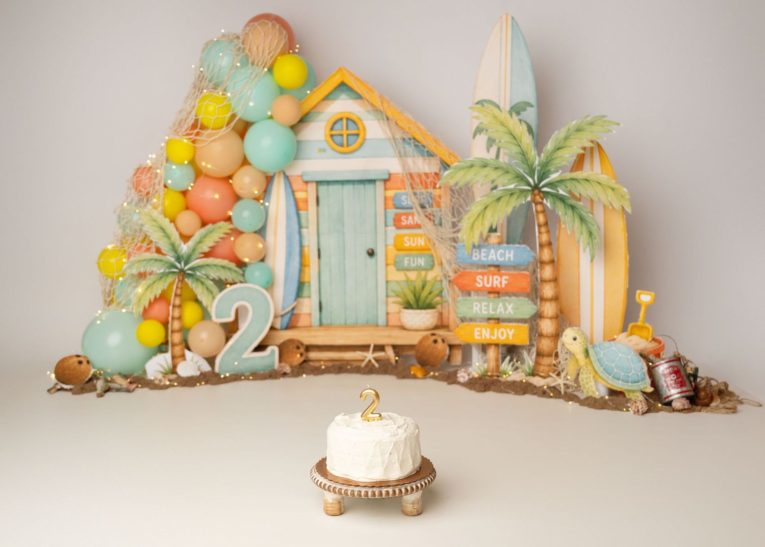Colorful first birthday cake smash photography setup with balloons and tropical decorations