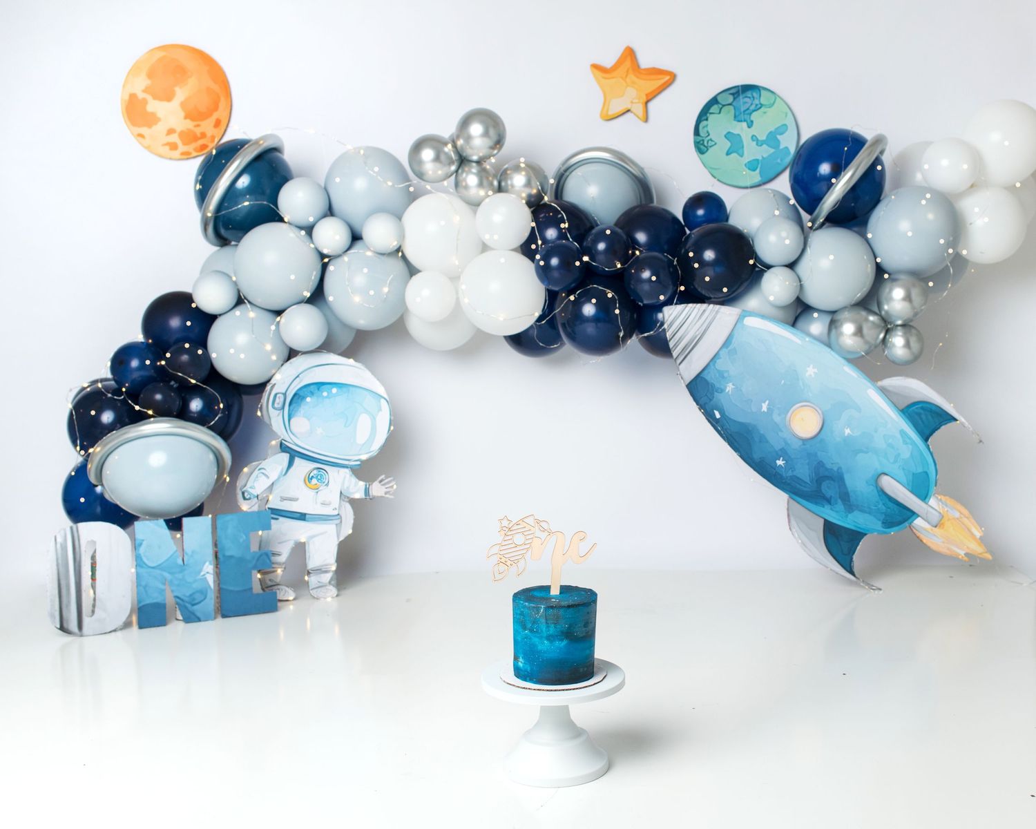 Space themed first birthday cake smash setup with navy, silver, and white balloons.