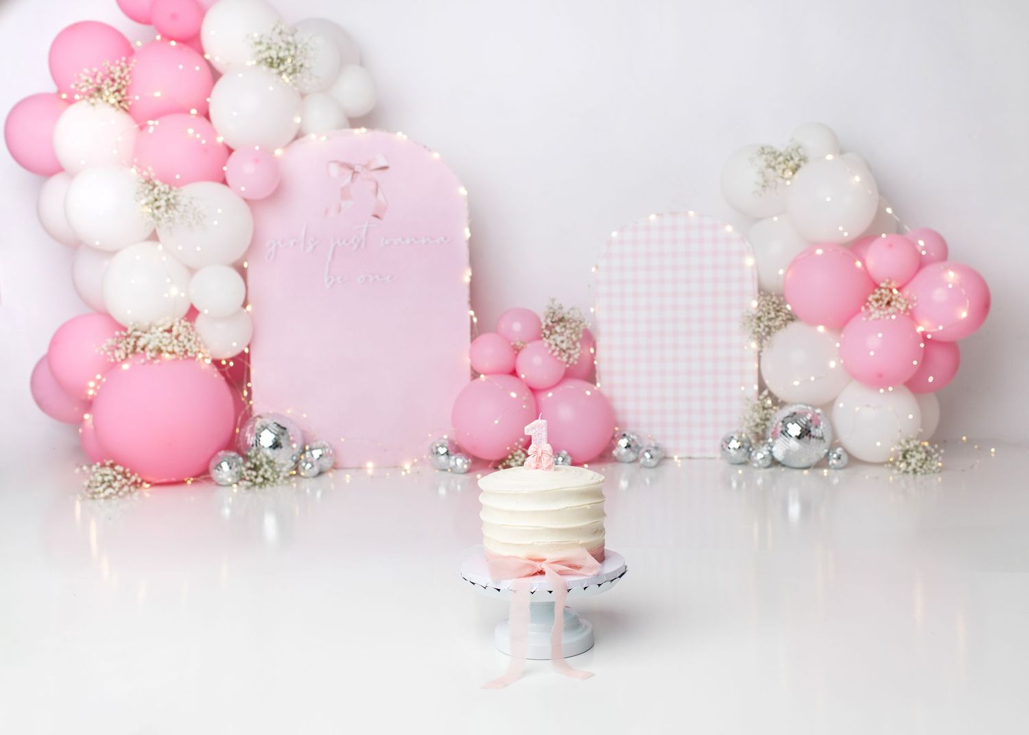 Pink floral first birthday cake smash setup with soft balloons and flowers.