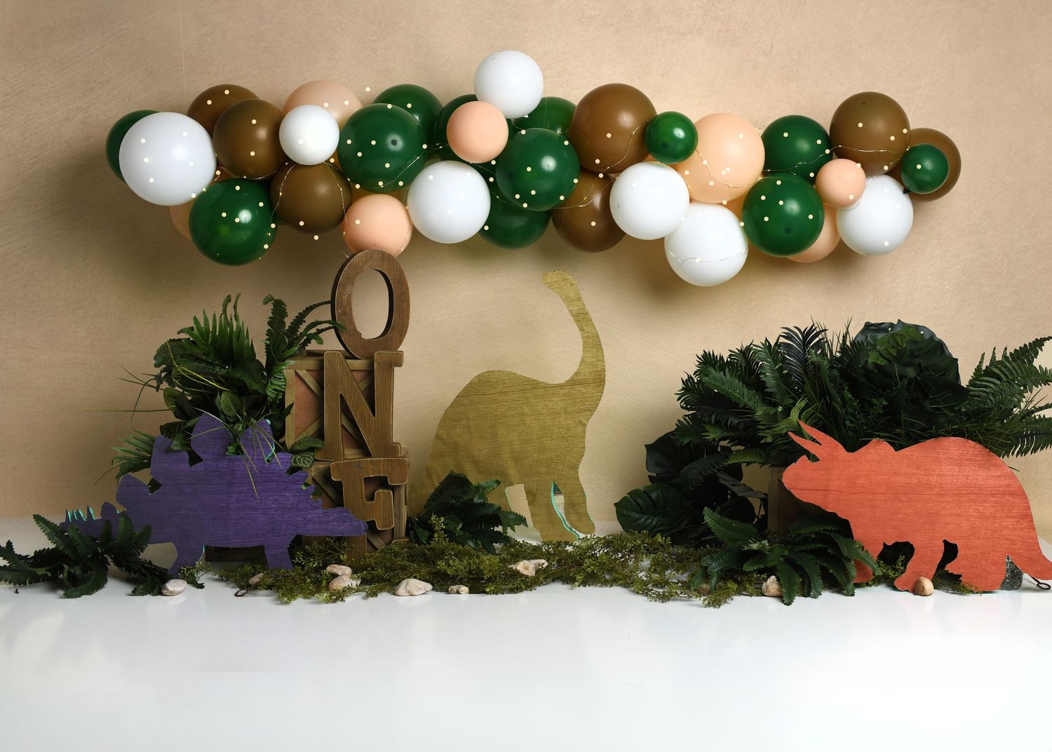 Dinosaur themed first birthday setup with green, brown, and orange balloon decor.