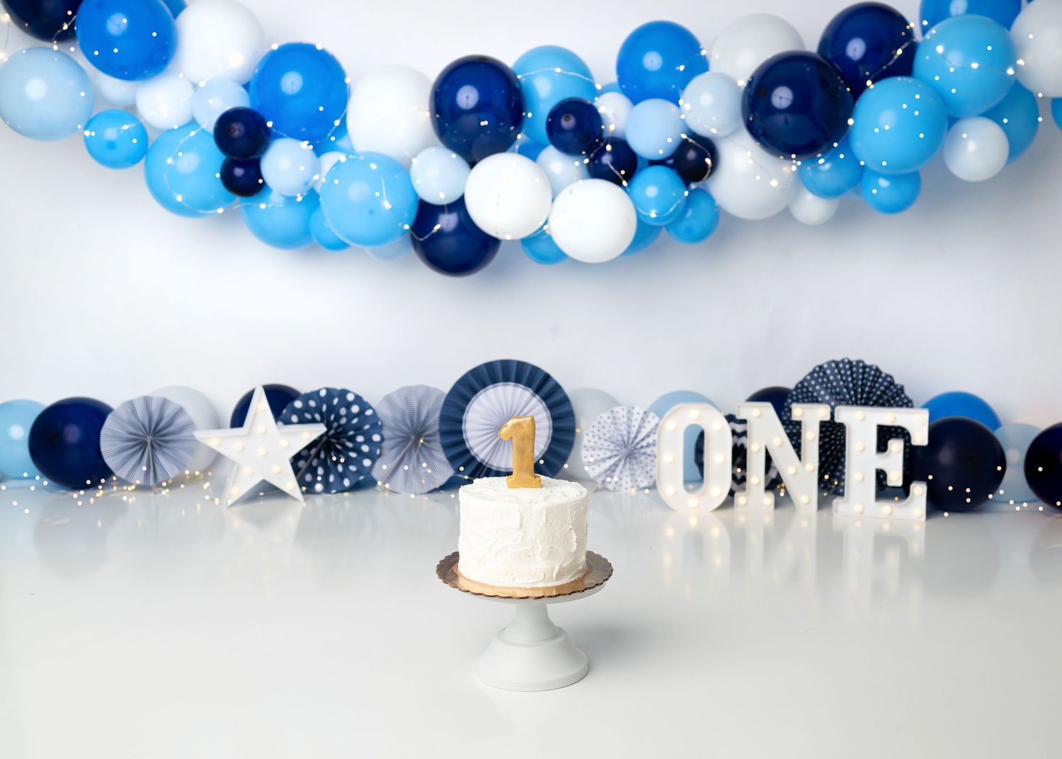 Blue and white first birthday cake smash setup with balloon garland.