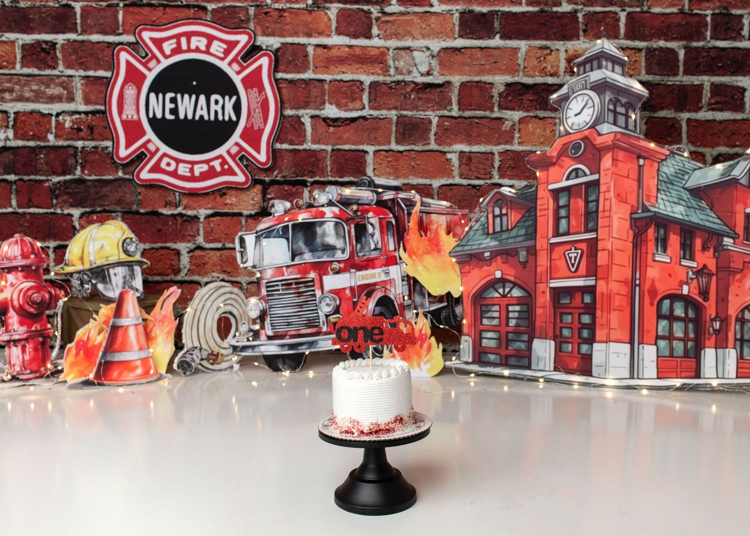 Firefighter themed first birthday cake smash setup with red brick backdrop in Linden, New Jersey.