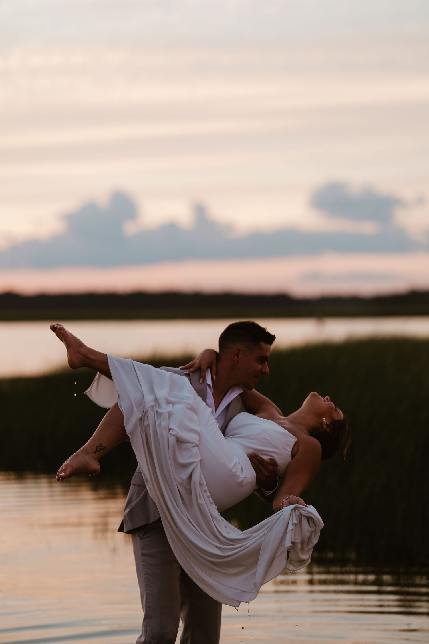 Romantic silhouette of couple dancing by the water at sunset.