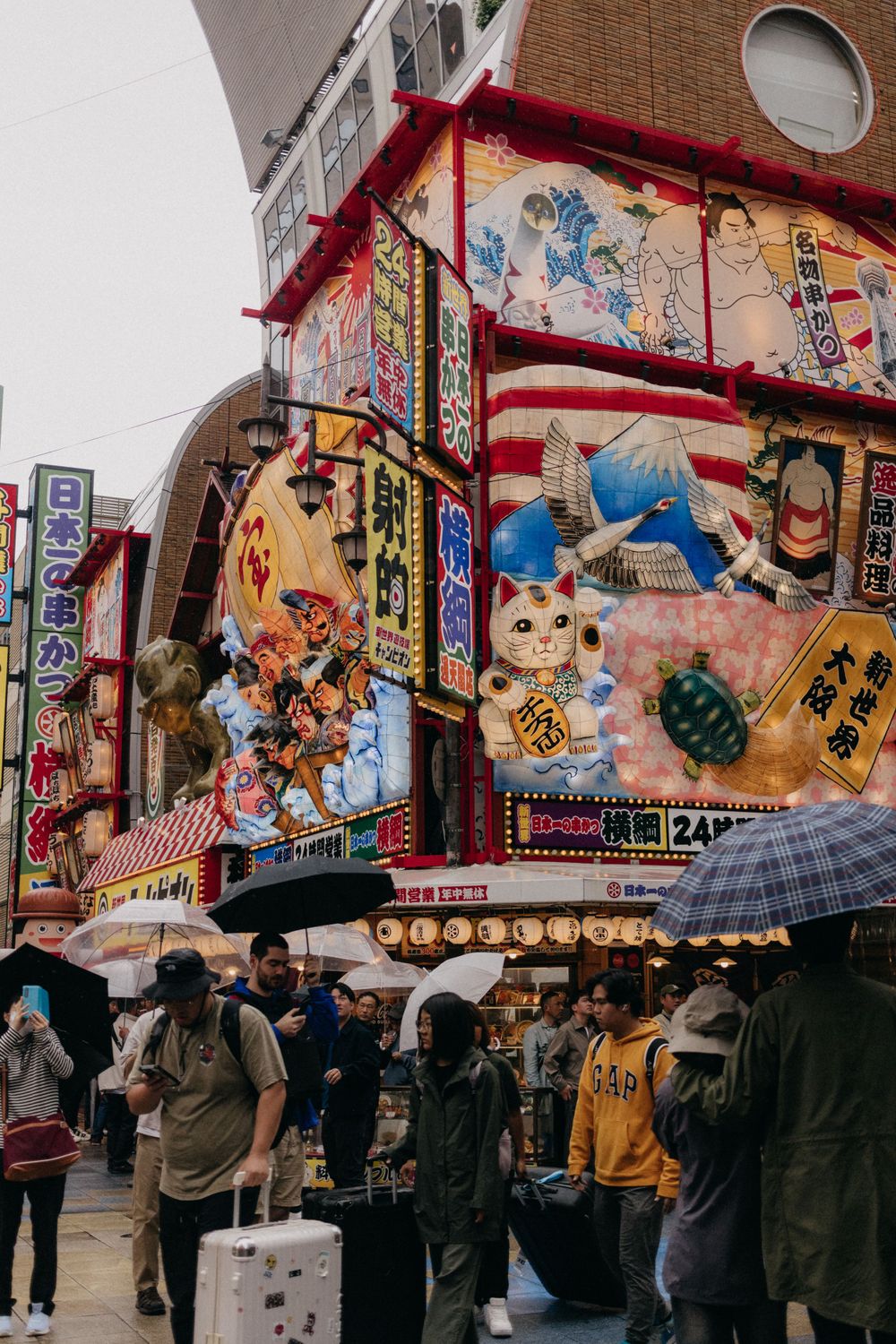Colorful Japanese store fronts with traditional artwork and lanterns in a bustling shopping district.