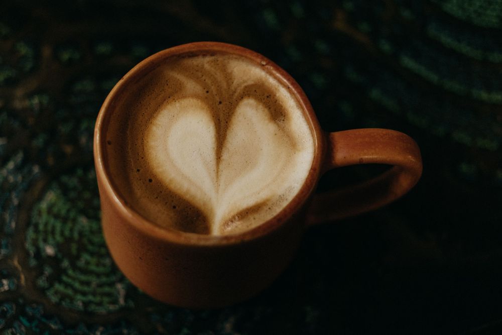 Coffee cup with heart-shaped latte art on dark background.