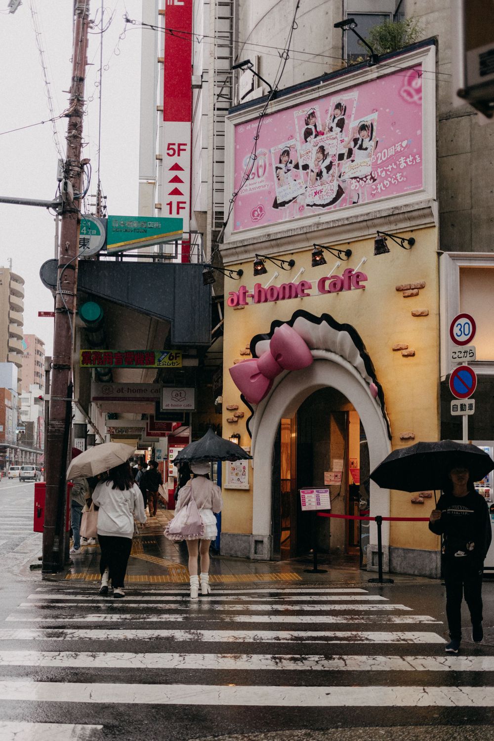 Pink-themed cafe entrance with cartoon character decor on a rainy street corner in Japan.