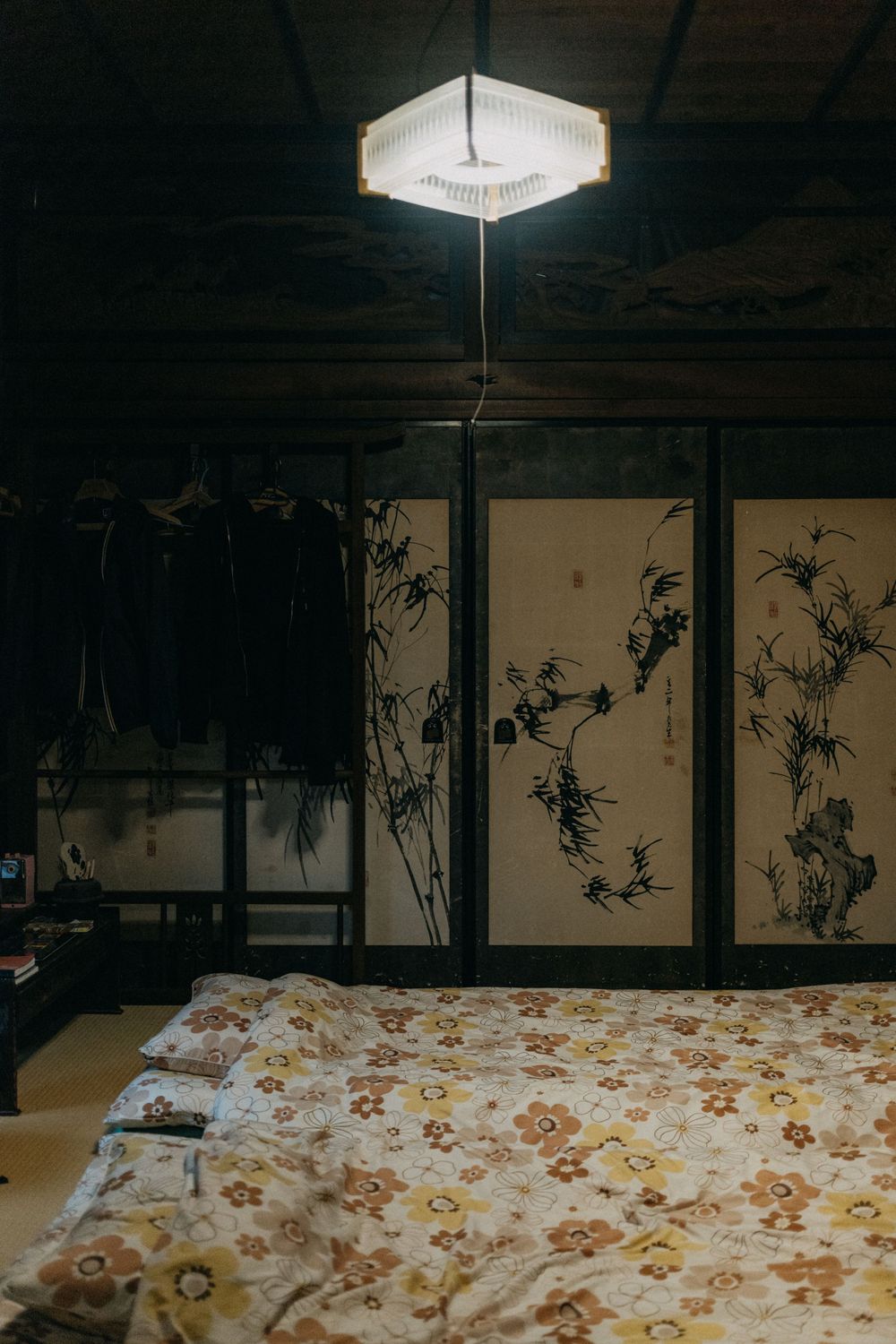 Traditional Japanese bedroom with floral bedding and ink paintings under dim lighting.