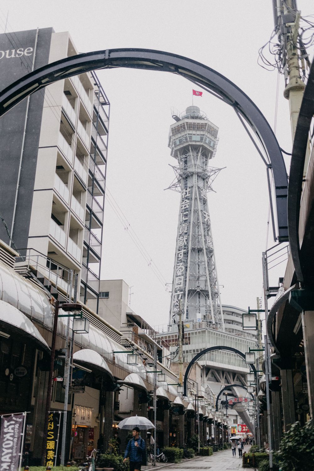 Tsutenkaku Tower in Osaka framed by an architectural arch on a rainy day.
