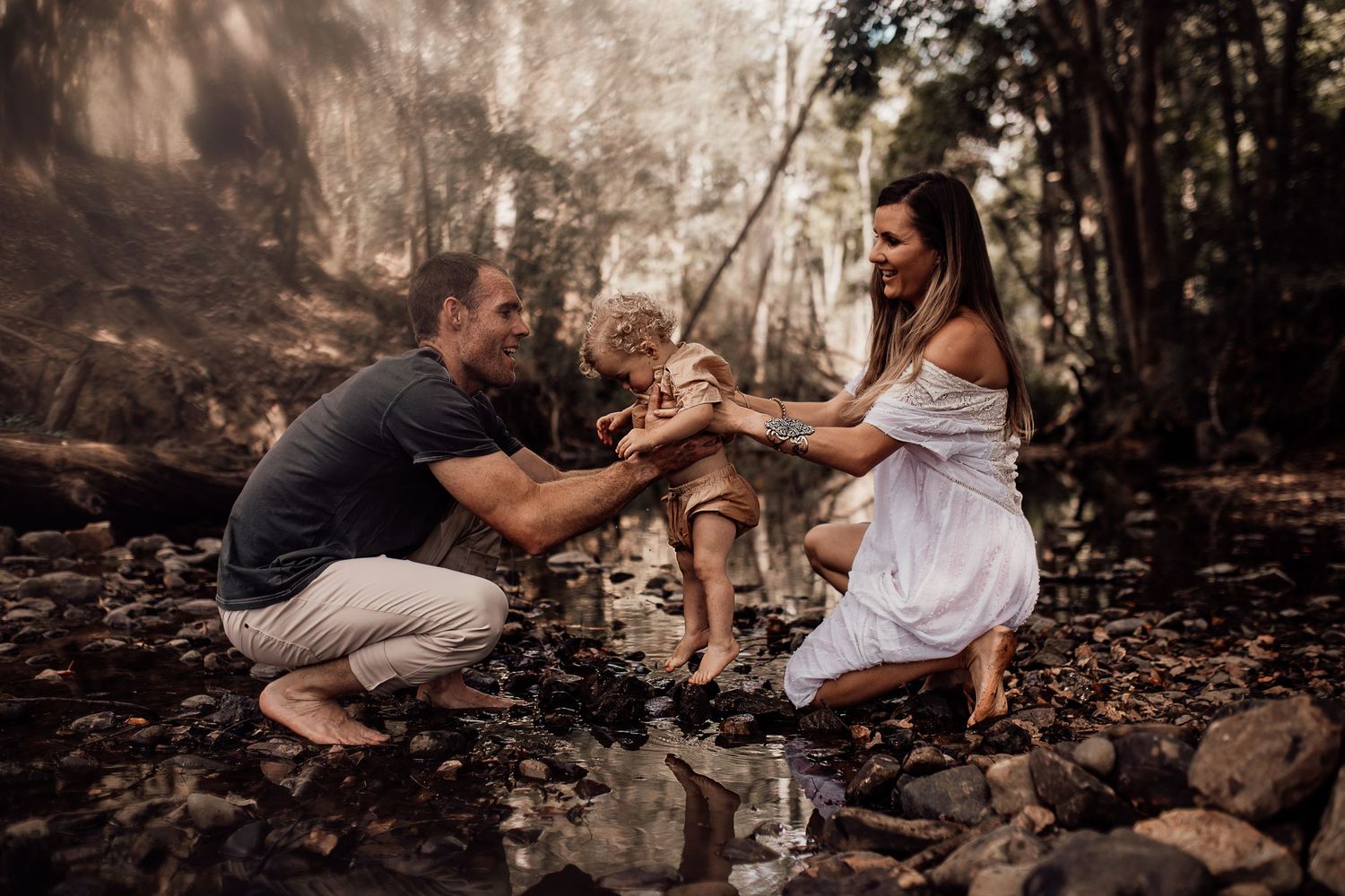 A family enjoys a playful moment together by a rocky stream in the woods.