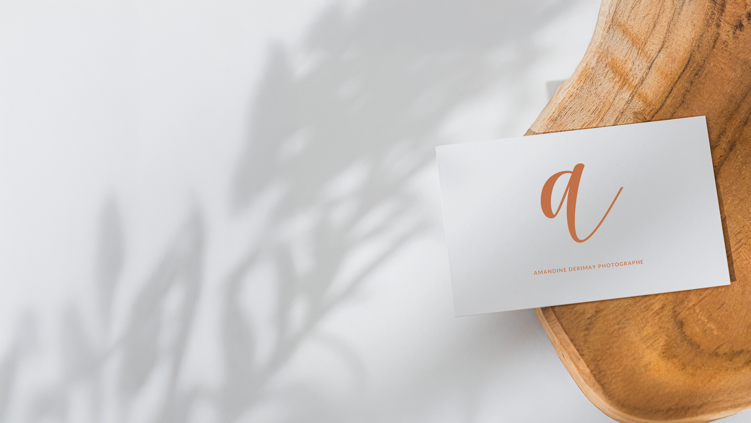 Minimalist business card with cursive letter 'a' on wooden surface.