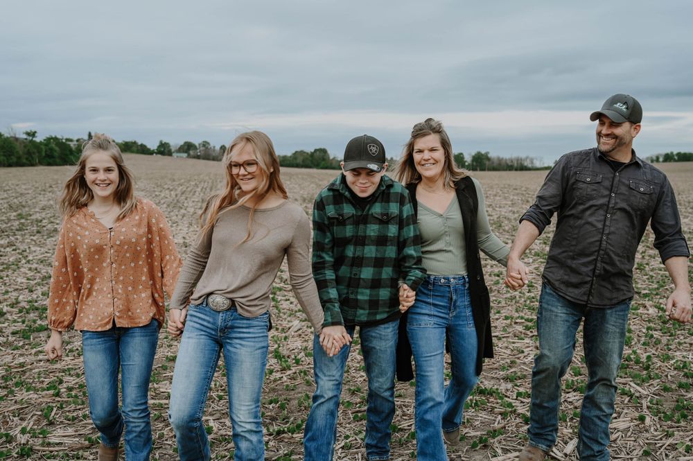 A group stands together holding hands while walking through an empty farm field on an overcast day.