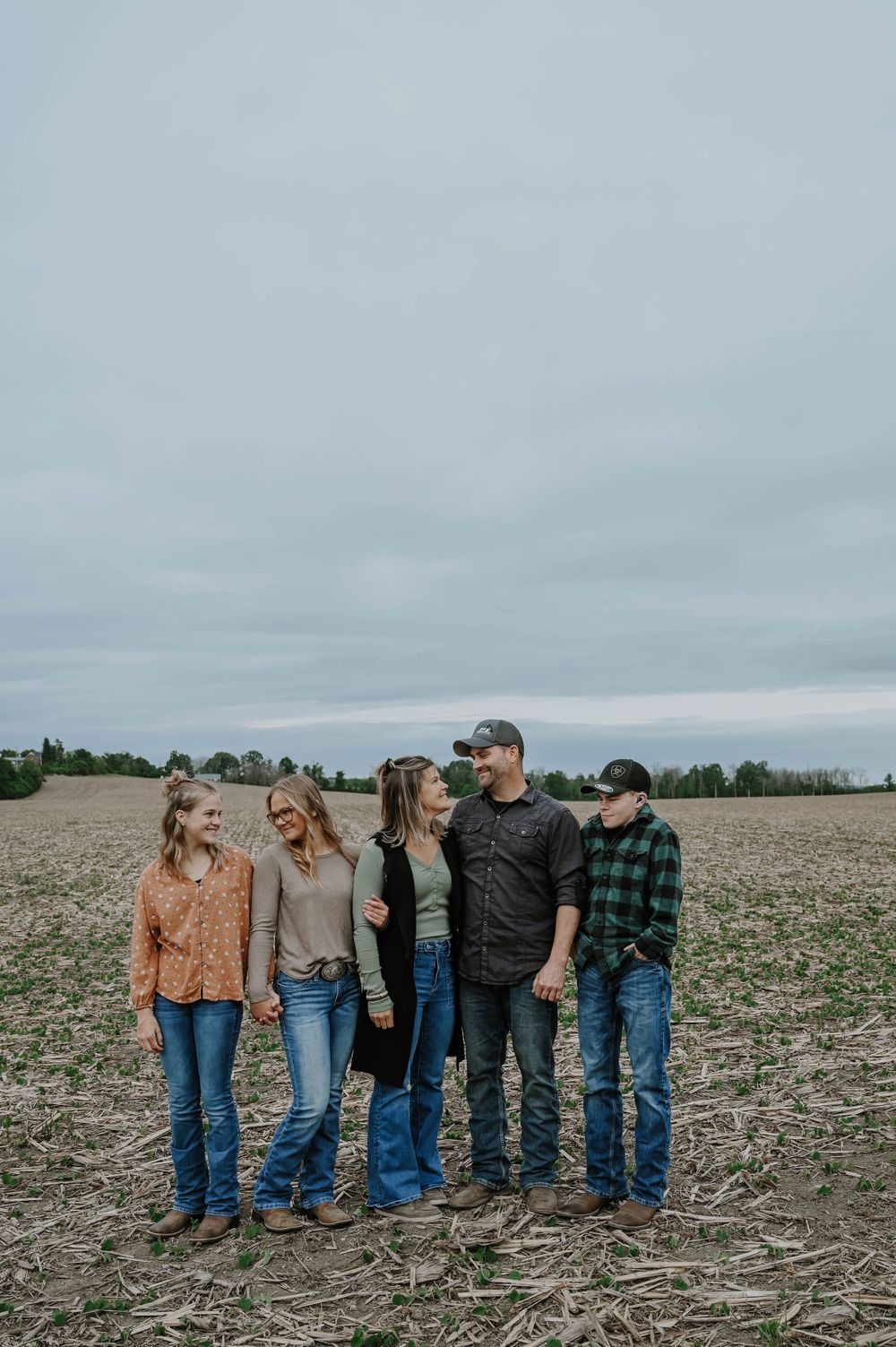 A group of five people standing together in casual attire on a harvested agricultural field under an overcast sky.