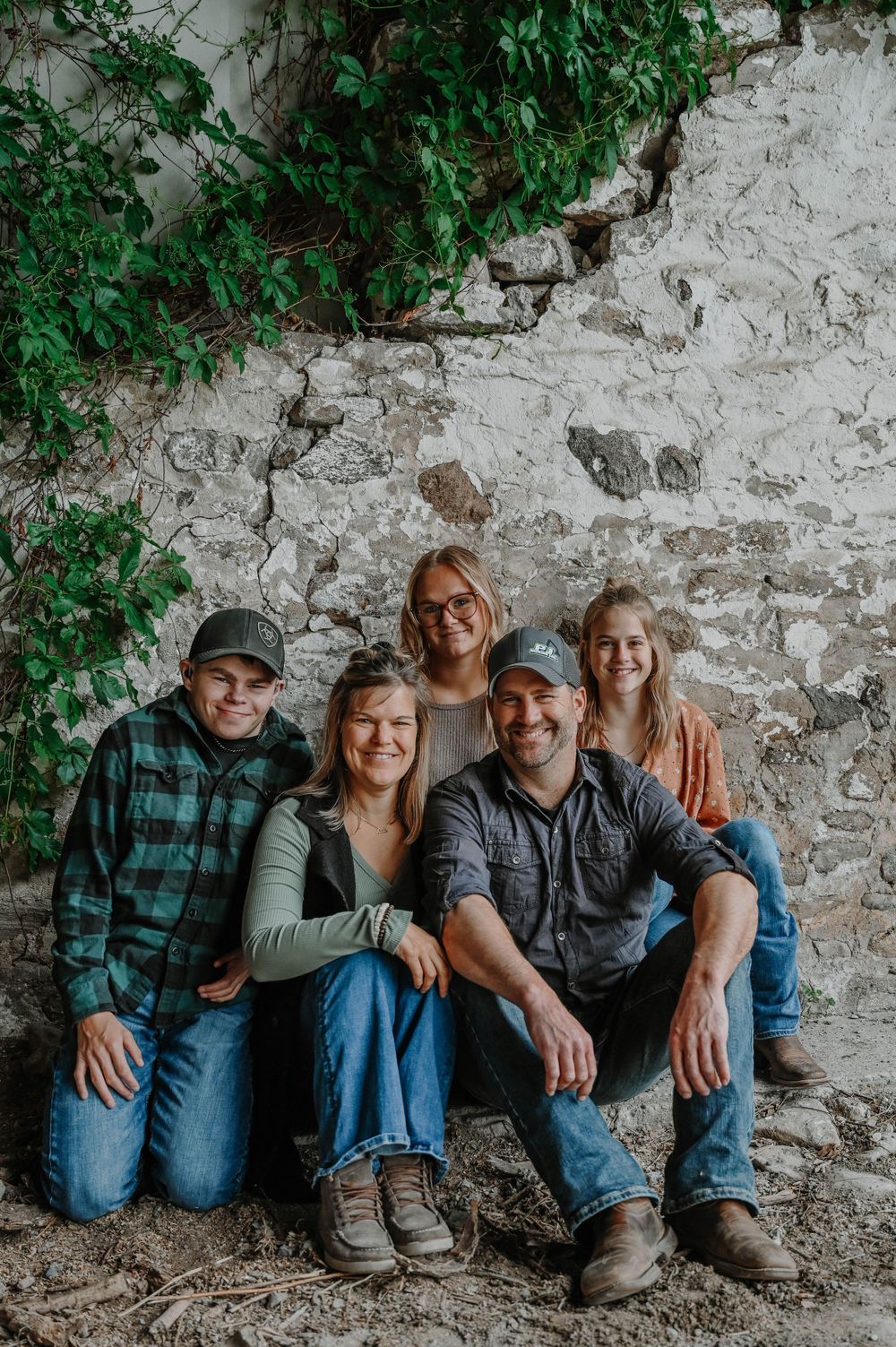 A family poses together in front of an old stone wall with green ivy growing on it.
