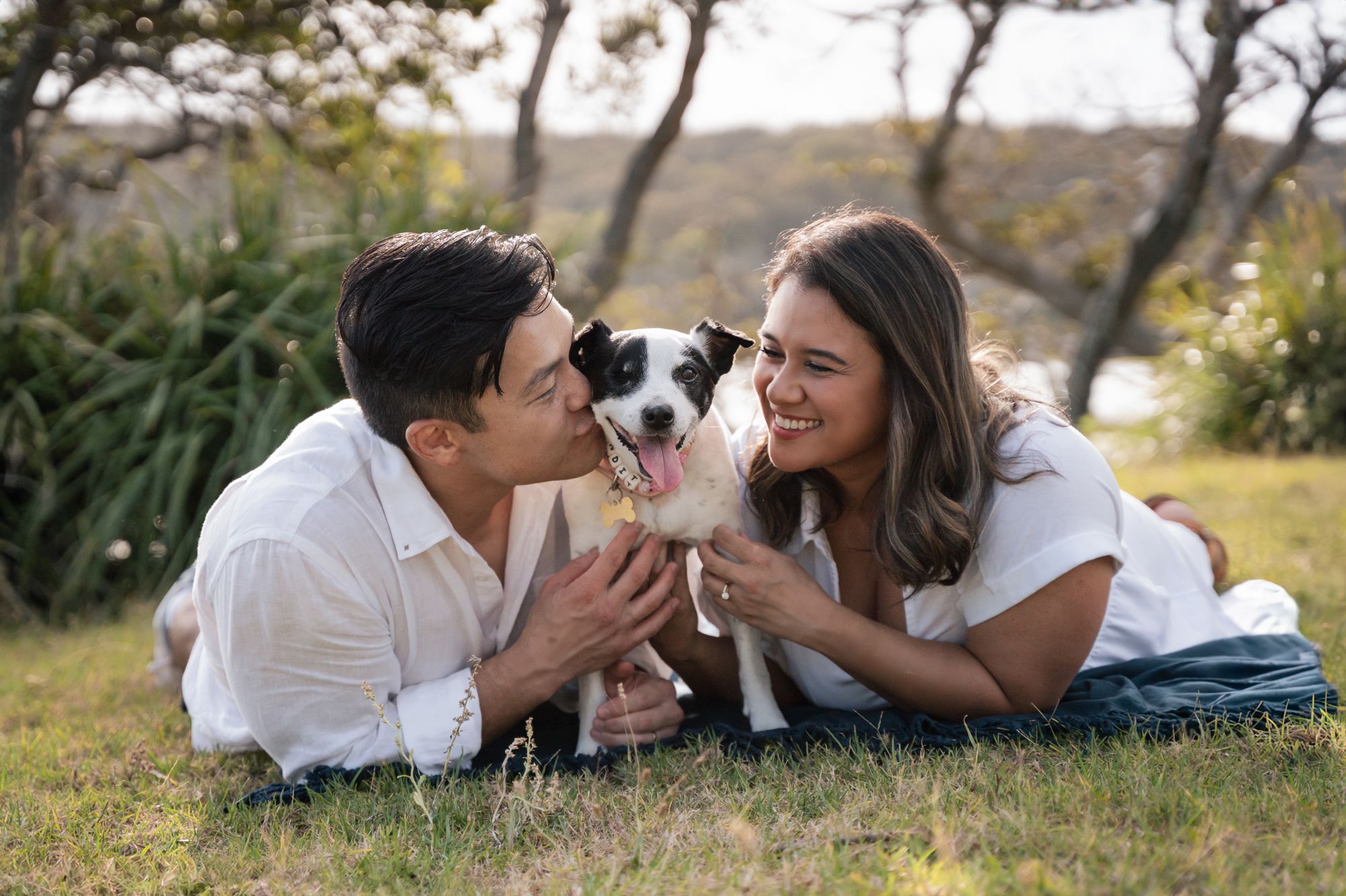 a couple with their dog laying on the grass having fun during a photoshoot in sydney