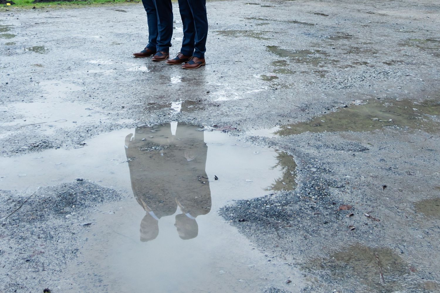 Reflection of figures in puddle on wet concrete pavement.