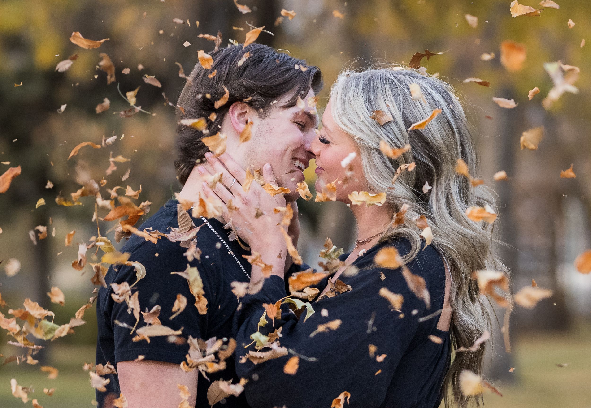 An affectionate moment captured with autumn leaves swirling around a couple outdoors.