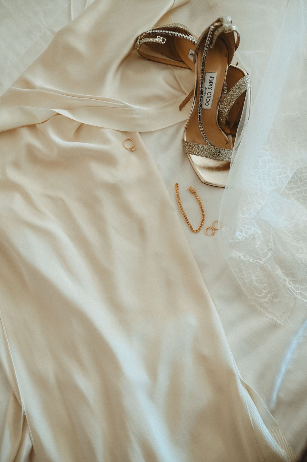 Elegant cream colored dress fabric alongside sparkly gold and white high heel slingback shoes with delicate jewelry.