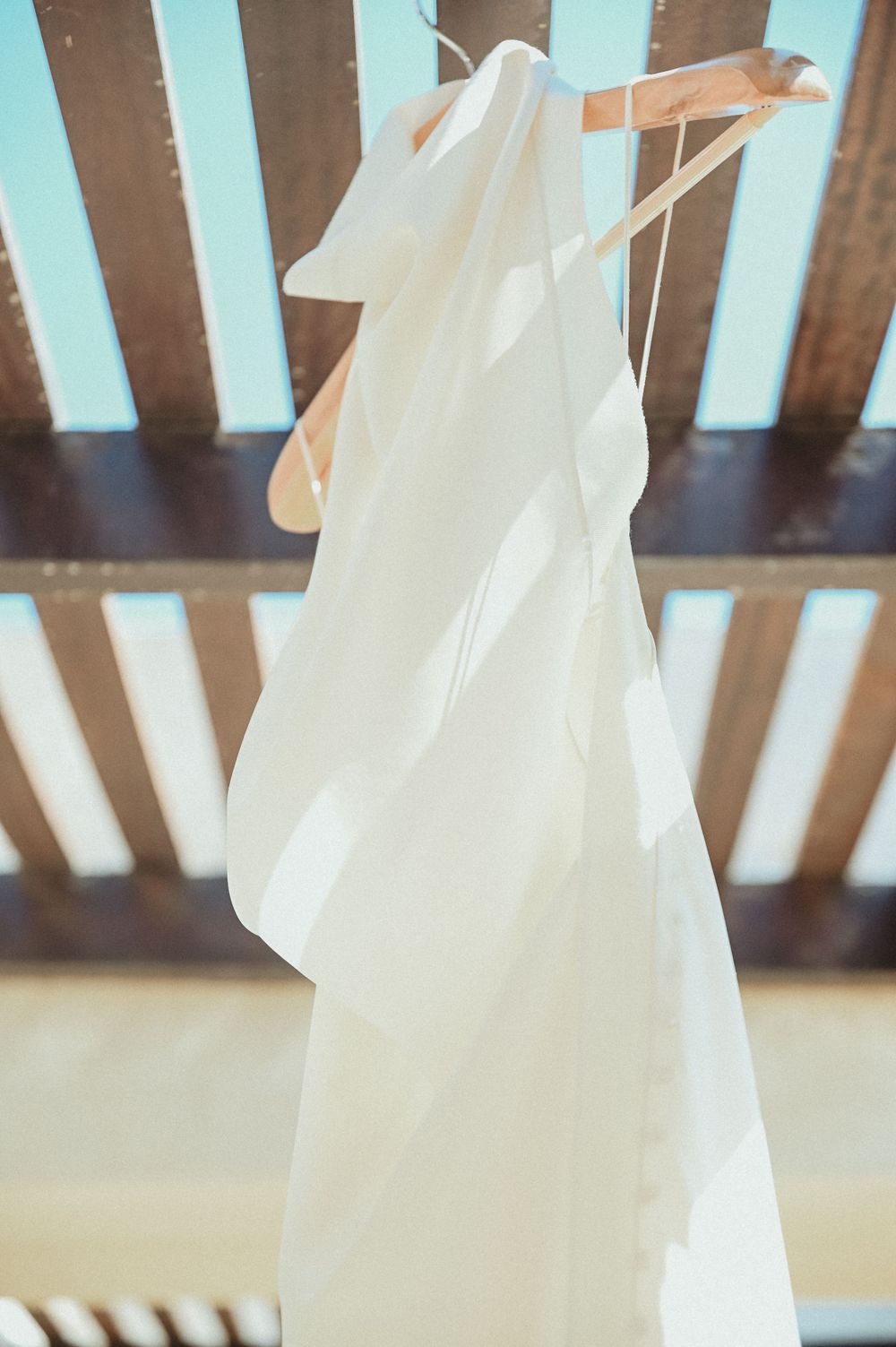 A white wedding veil hangs elegantly from a wooden pergola or beam in natural lighting.