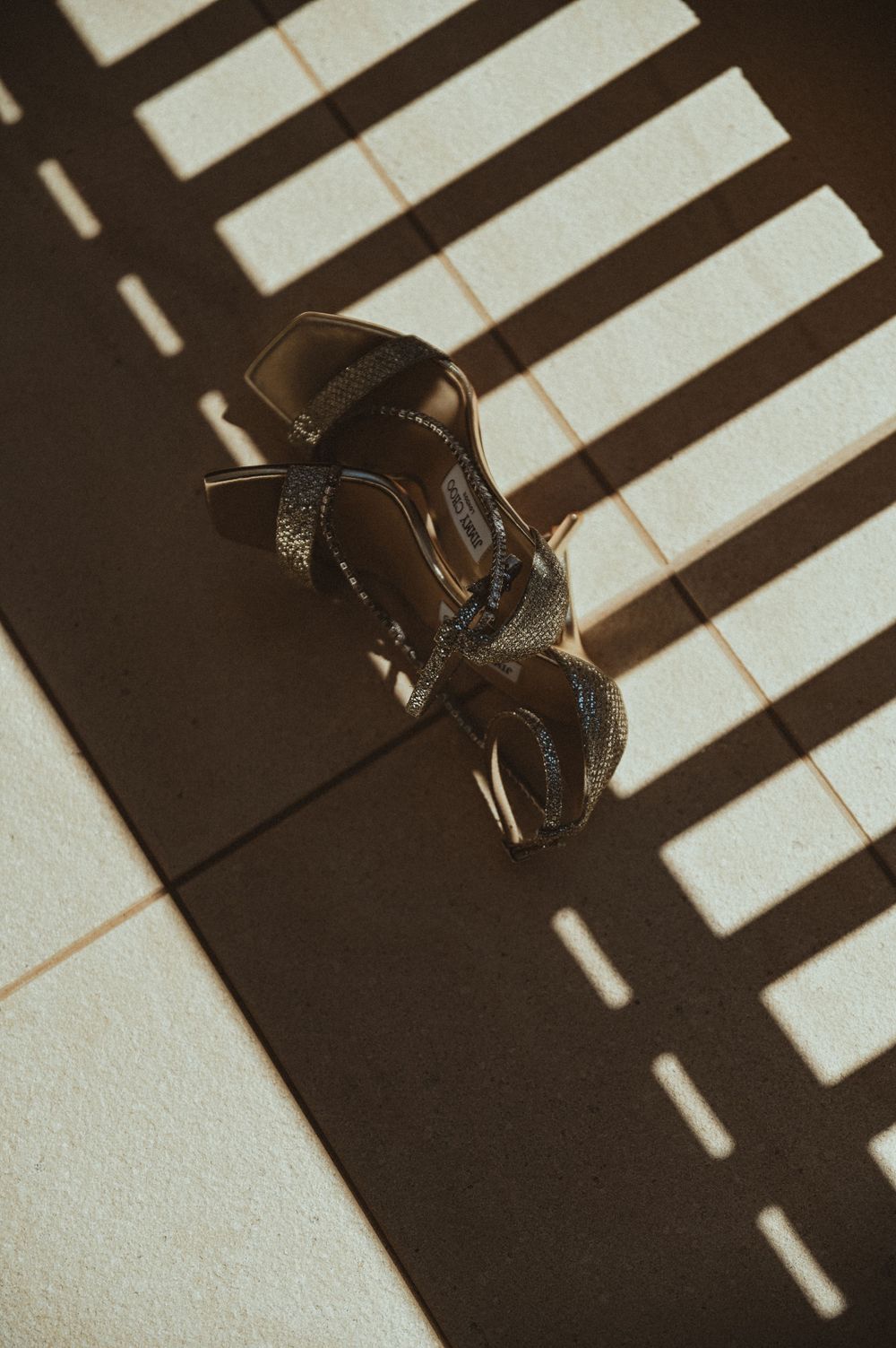 Vintage toy car photographed from above on a white surface with dramatic window blind shadows creating striped pattern.
