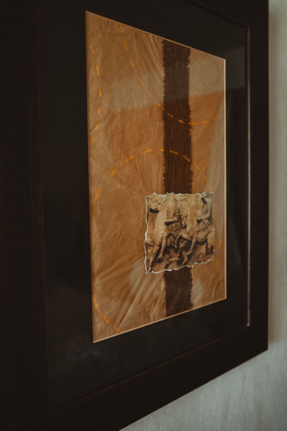 A framed abstract artwork featuring a brown and beige textured surface with a small rough-edged paper element in the center.