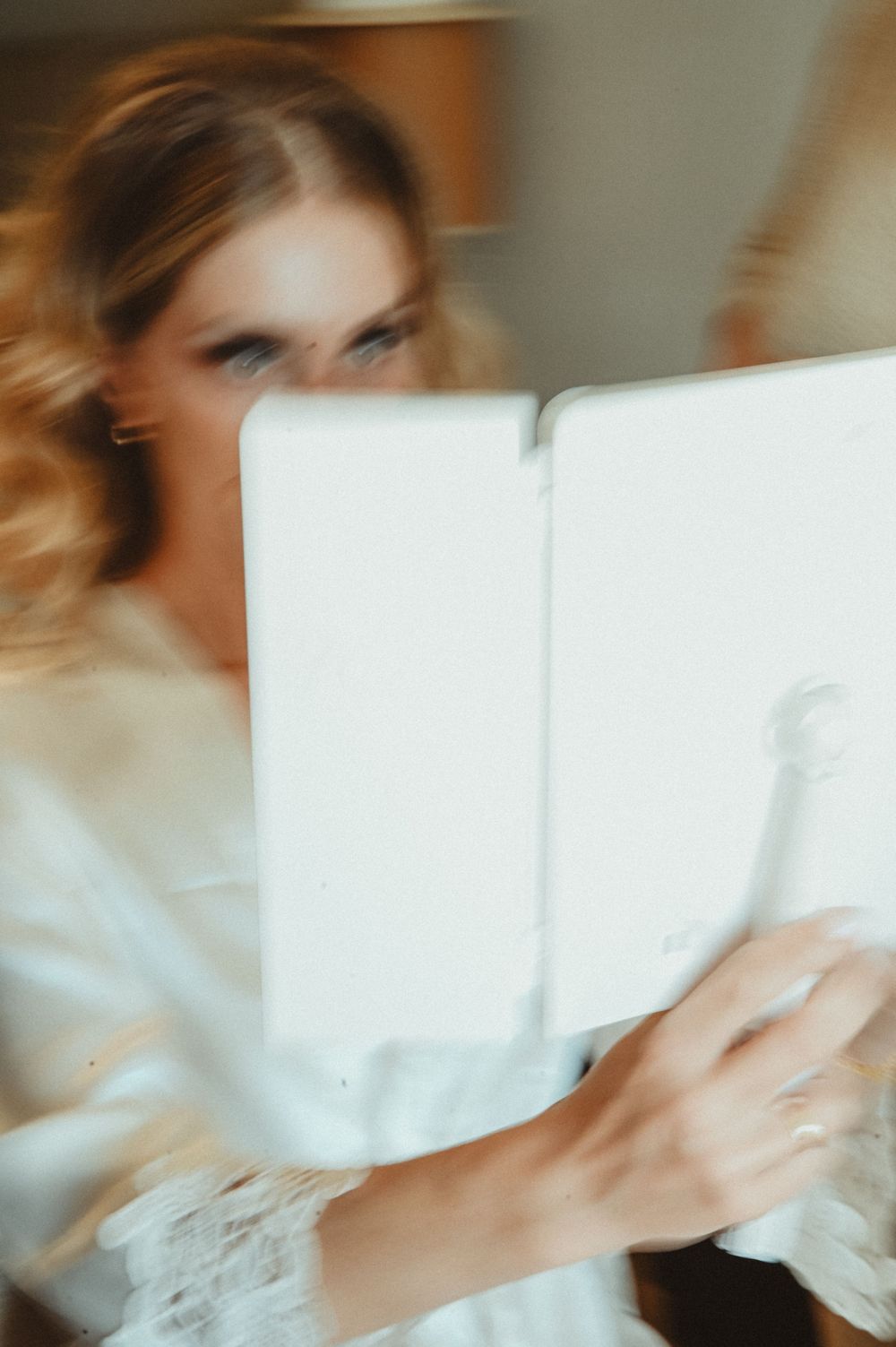 Soft focus image of someone holding a white book or tablet in natural lighting.
