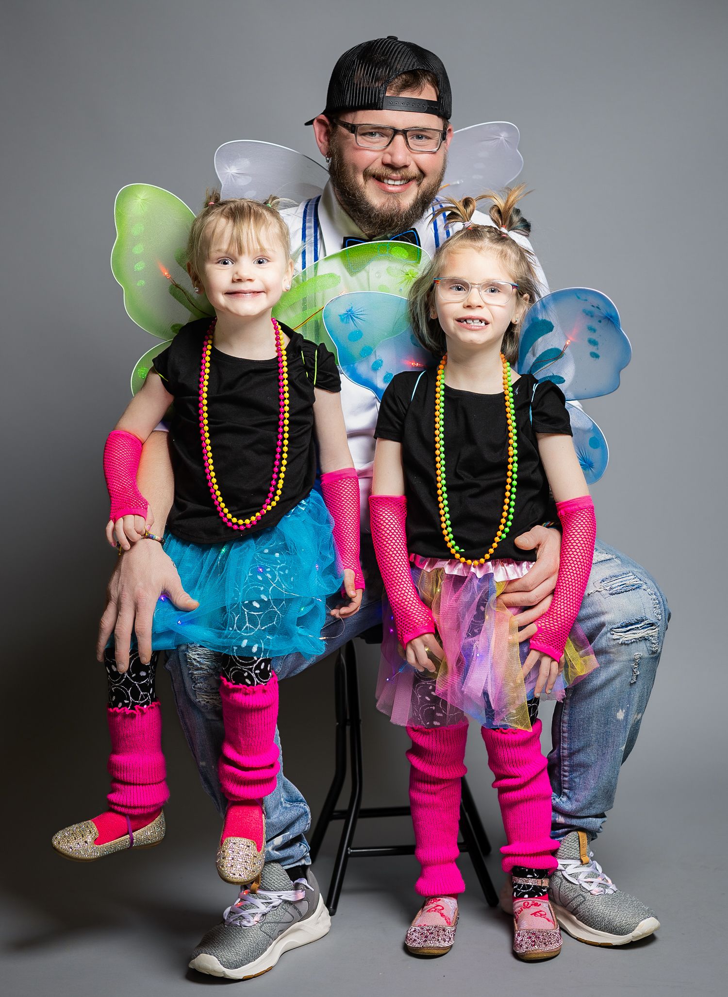 Parent and children wearing fairy wings and colorful costumes pose for playful portrait.
