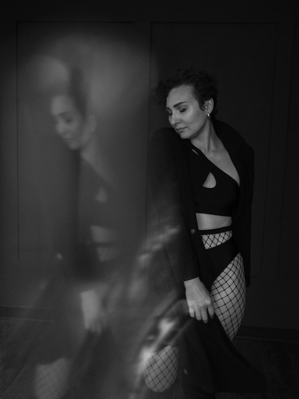 Artistic black and white portrait with a reflection effect showing a figure in fishnet stockings and dark clothing  in Bellevue studio..