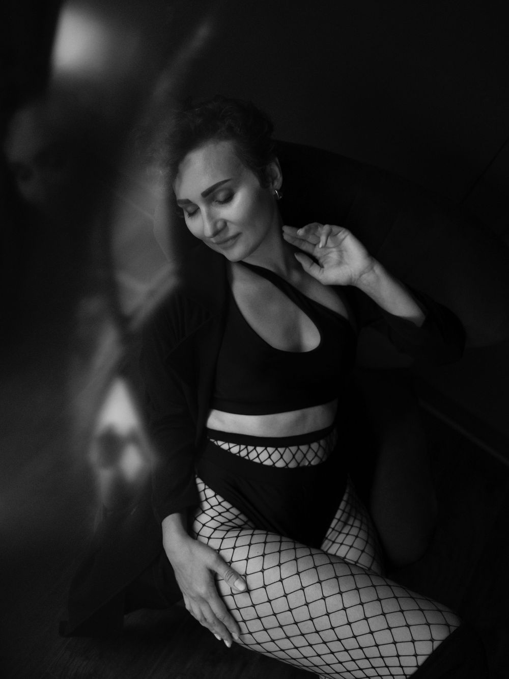 Artistic black and white portrait photo of a dancer in a black outfit and fishnet stockings posing gracefully in dark lighting  in Bellevue.