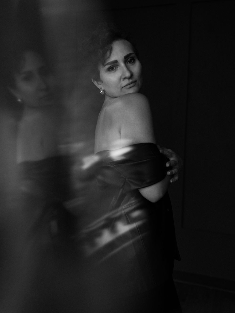 Dramatic black and white portrait showing figure wrapped in dark fabric with shoulder exposed, creating moody artistic effect  in Bellevue .