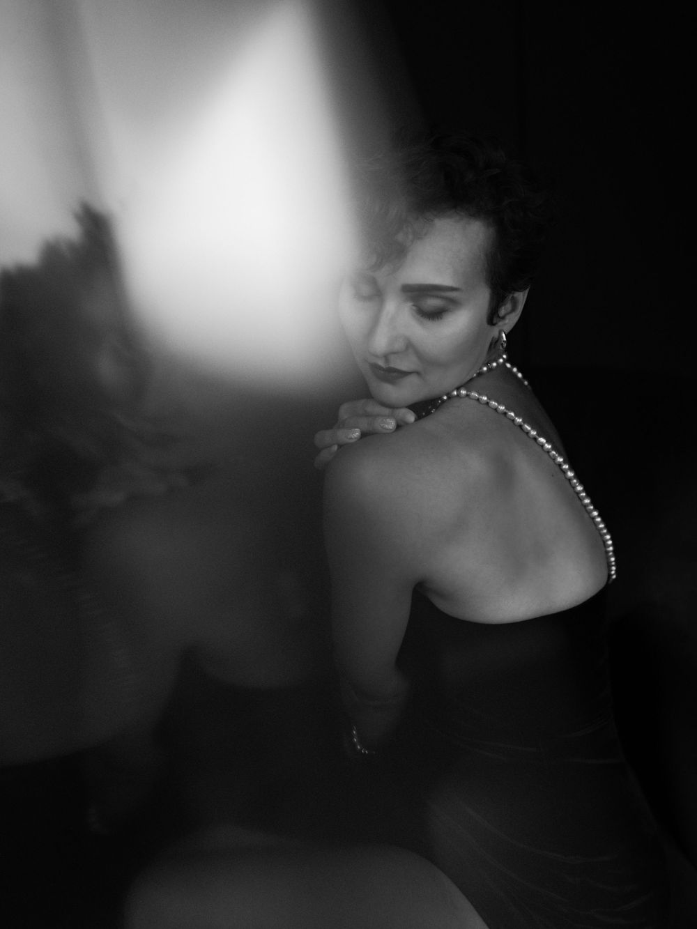 Artistic black and white portrait of a figure in dark attire wearing a pearl necklace with dramatic lighting  in Bellevue studio..