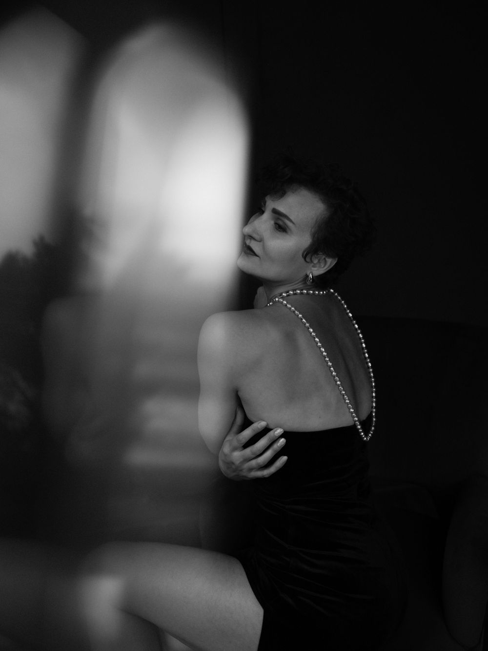 A dramatic black and white portrait shows an elegant figure in a strapless dress with draped pearls across their bare back  in Bellevue.