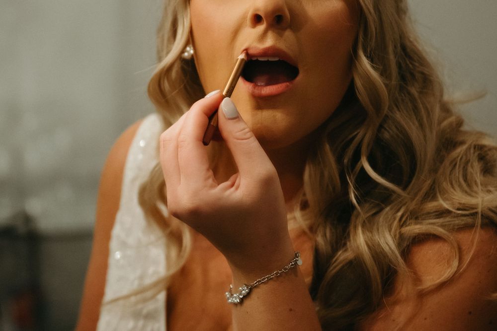 Close up of applying lipstick while wearing a delicate necklace and sparkling earrings.