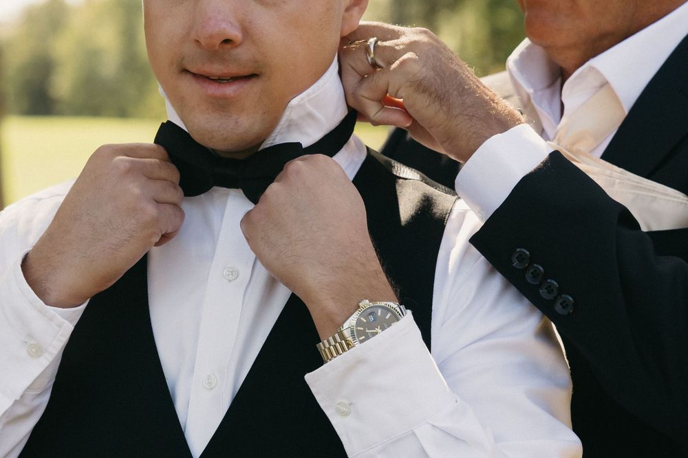 Close-up shot of hands adjusting a black bowtie on formal attire with a watch visible.