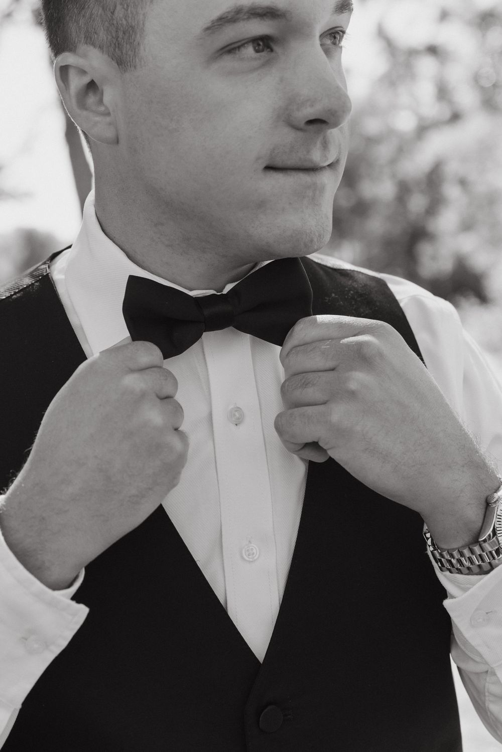 Black and white photo of formal attire with focus on adjusting a classic bow tie.