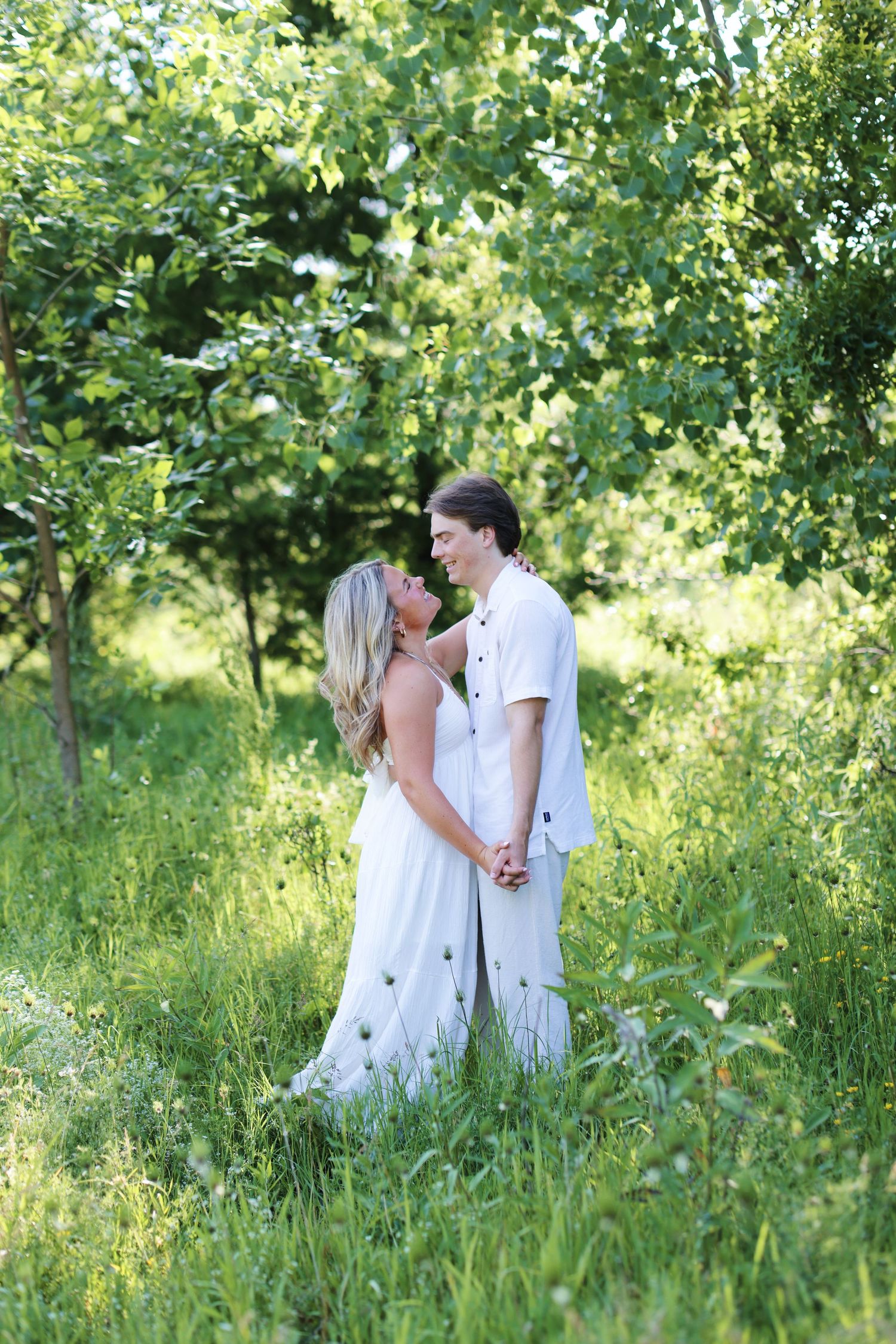 Couple holding hands while walking through beach grass at sunset.