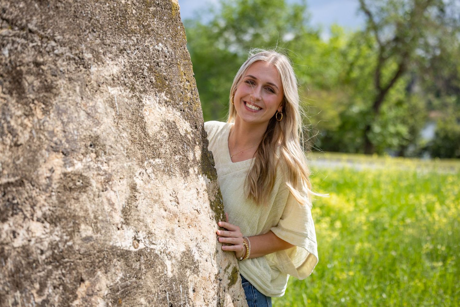 Person poses beside large rock formation in sunny spring meadow.