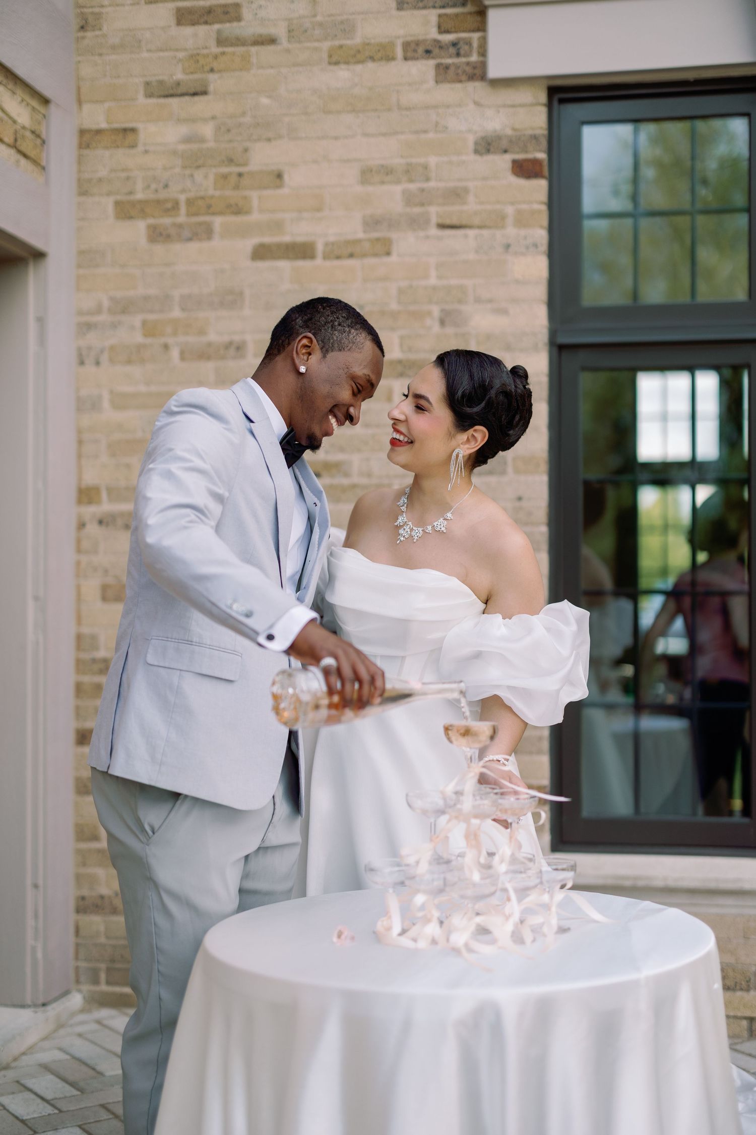 A bride and groom share a kiss while holding champagne glasses at their wedding celebration.